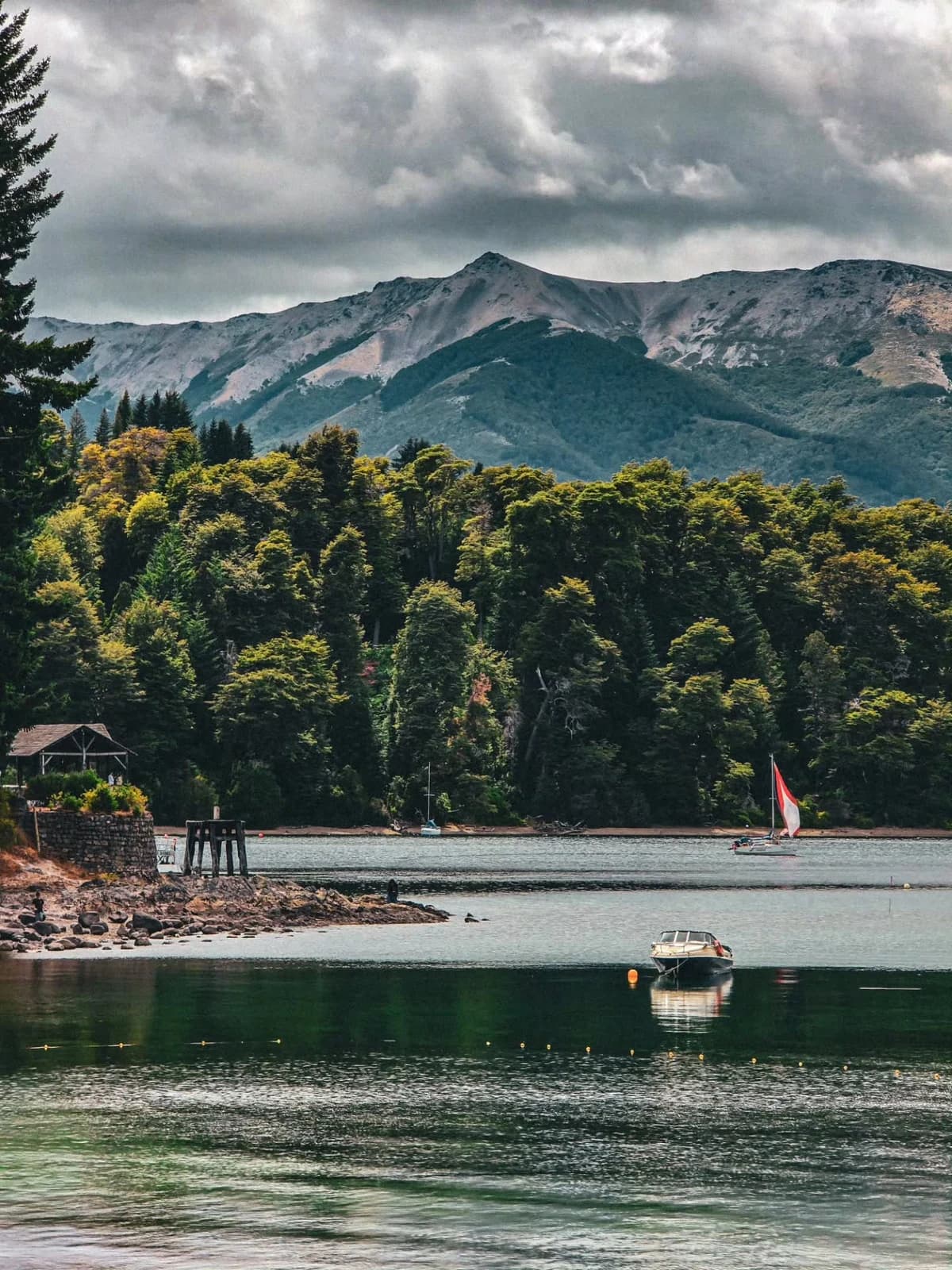A boat on a Patagonian lake with forest and mountains under a cloudy sky